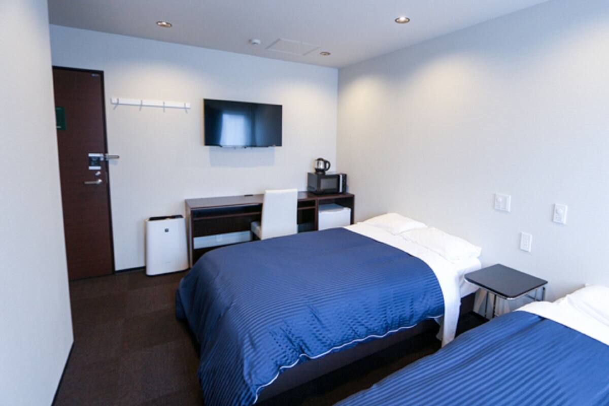 A hotel room with two beds, a desk, a television, and a microwave.