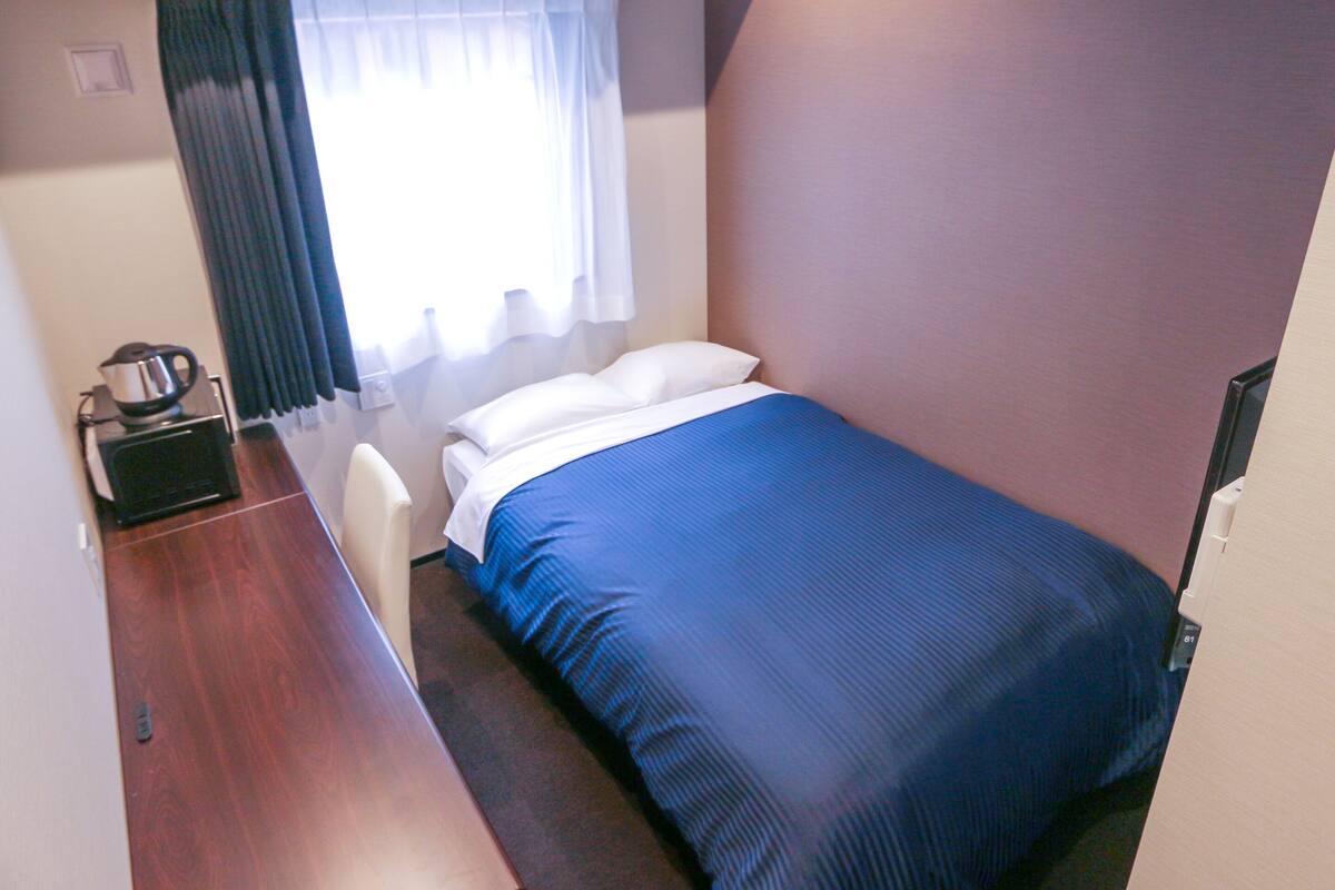 A small, compact room with a single bed, a desk, and a chair.