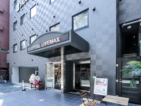 A hotel entrance with a checkered facade, a sign reading "HOTEL LIVEMAX", and a wooden bench outside.