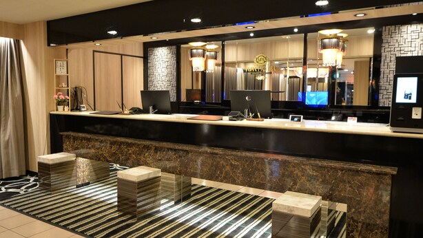A hotel reception area with a marble counter, a large mirror, and a modern chandelier. - APA Hotel Saitama Ageo Ekimae (Ageo)
