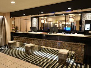 Ein Hotel-Empfangsbereich mit Marmor-Theke, einem großen Spiegel und einer modernen Kronleuchter.