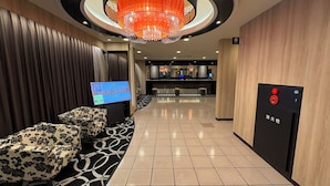 A hotel lobby with a reception desk, a large screen displaying information, a chandelier, and a fire alarm. - APA Hotel Saitama Ageo Ekimae (Ageo)