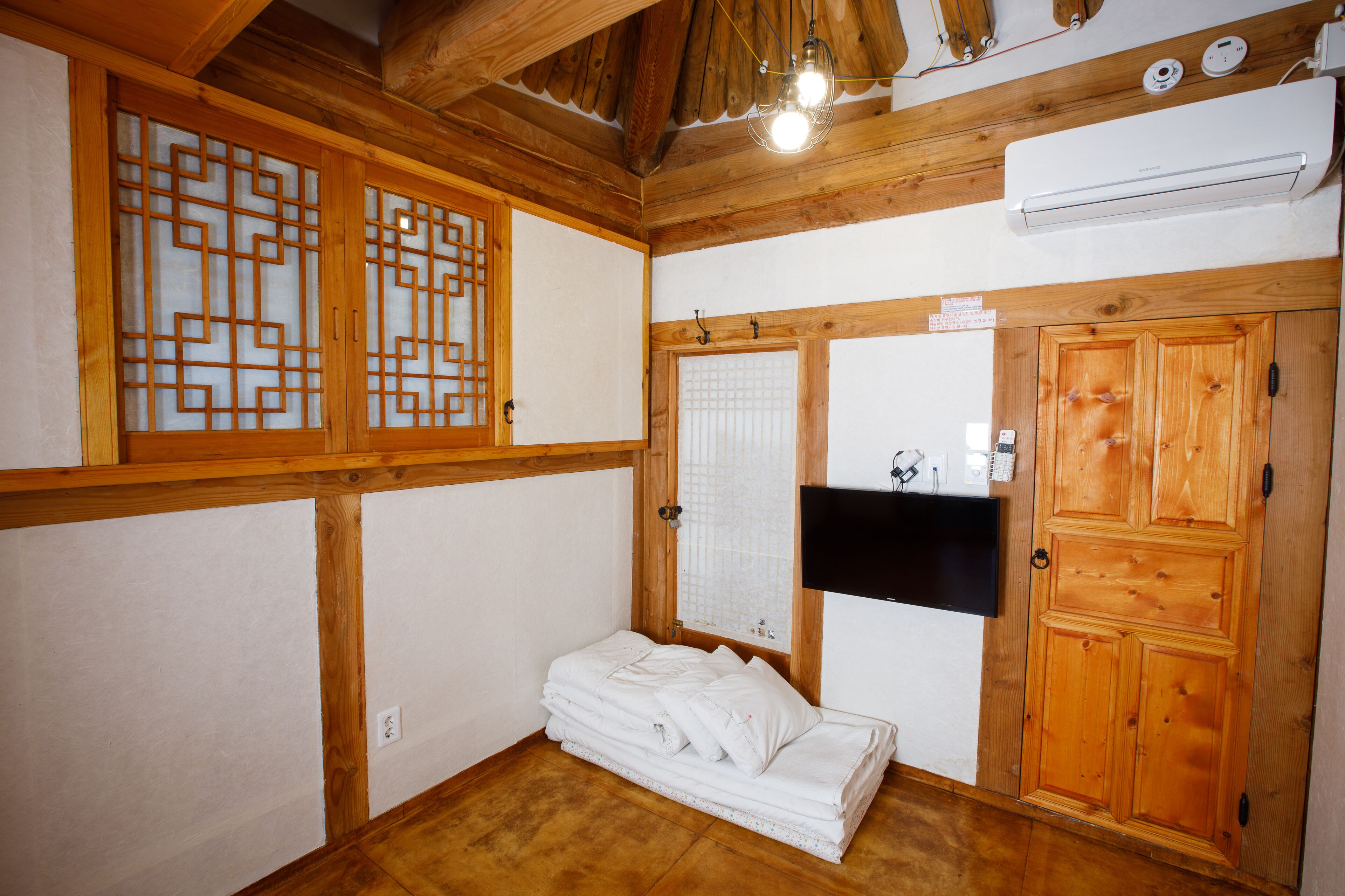 Een traditionele Japanse kamer met houten balken, tatami vloerbedekking, een shoji schuifwand en een wandgemonteerde televisie.