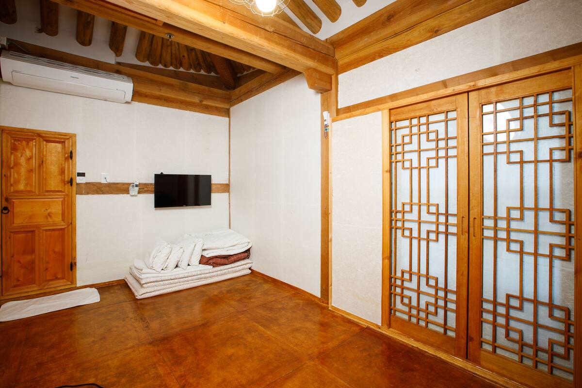 Une pièce avec des poutres apparentes, un téléviseur fixé au mur, une porte en bois et une porte coulissante traditionnelle ornée de motifs géométriques.