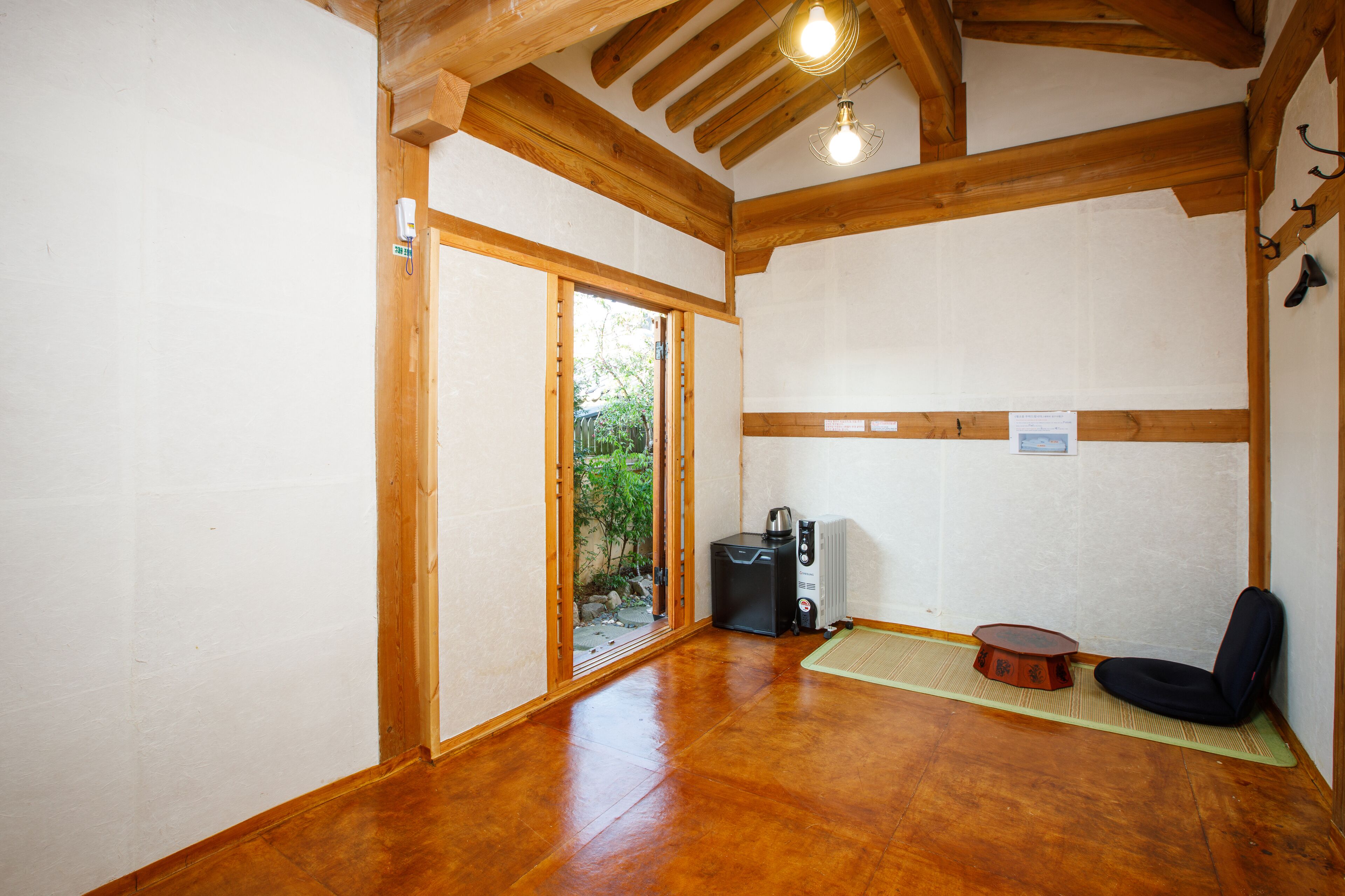 A room with wooden beams, a sliding door to a garden, a black heater, a black chair, and a small table.