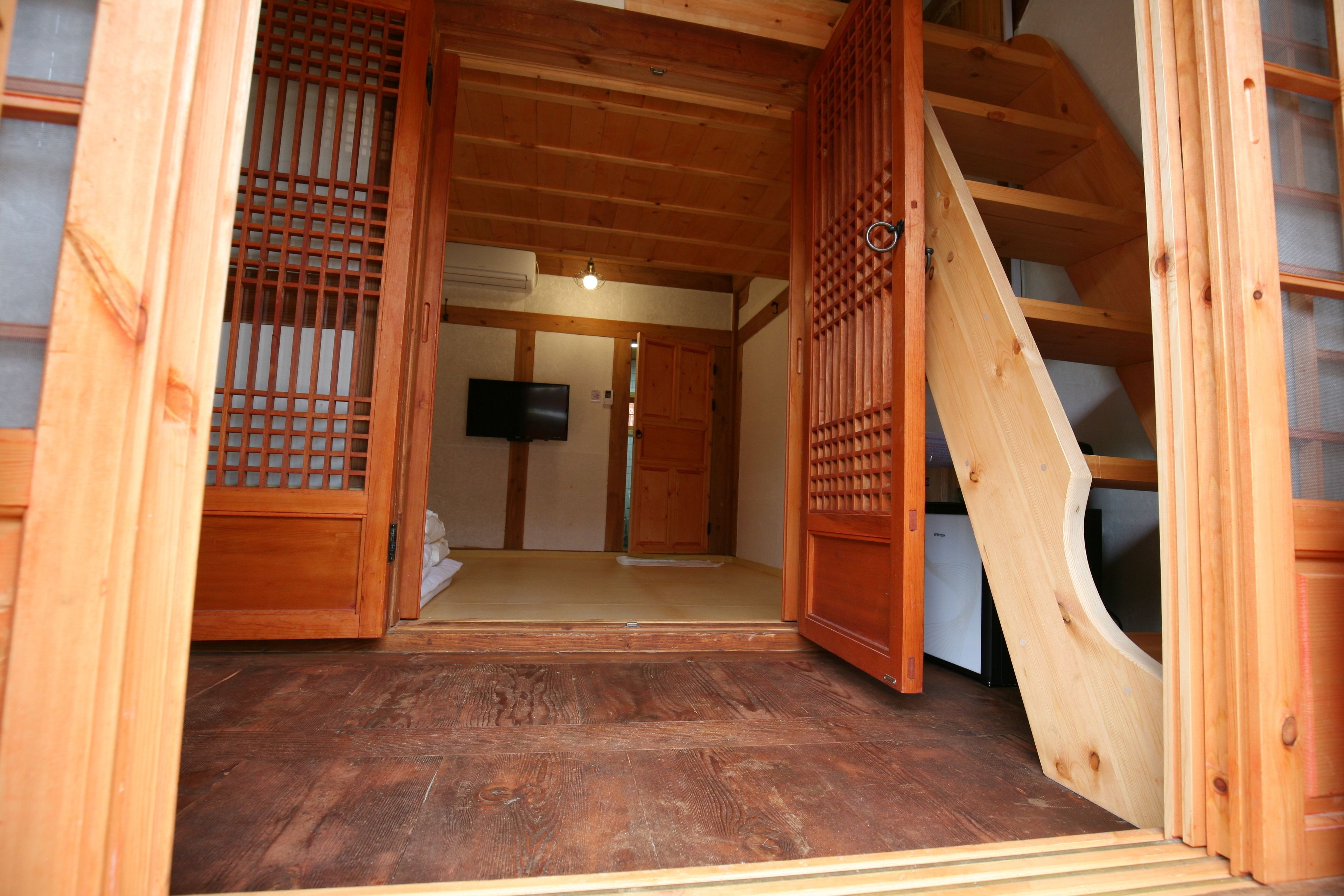 A traditional wooden interior with a tatami mat floor, a sliding door, and a television mounted on the wall.