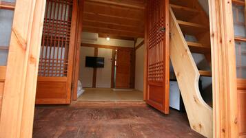 A traditional wooden interior with a tatami mat floor, a sliding door, and a television mounted on the wall.