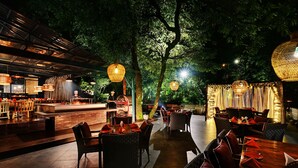An outdoor restaurant with wicker furniture, a bar area, and hanging lanterns. - Ayar Jungle Resort (Nainital)