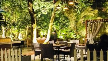 An outdoor dining area with tables and chairs, surrounded by trees and a white picket fence.