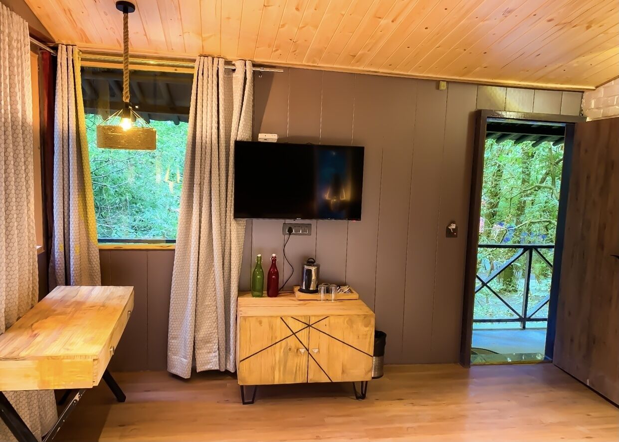 A wooden cabin interior with a TV mounted on the wall, a wooden table, and a cabinet with bottles and glasses.