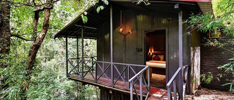 A rustic wooden cabin with a balcony, surrounded by dense forest.