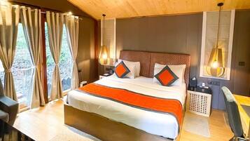 Quarto com teto de madeira, cama com roupa de cama laranja, escrivaninha e uma cadeira.
