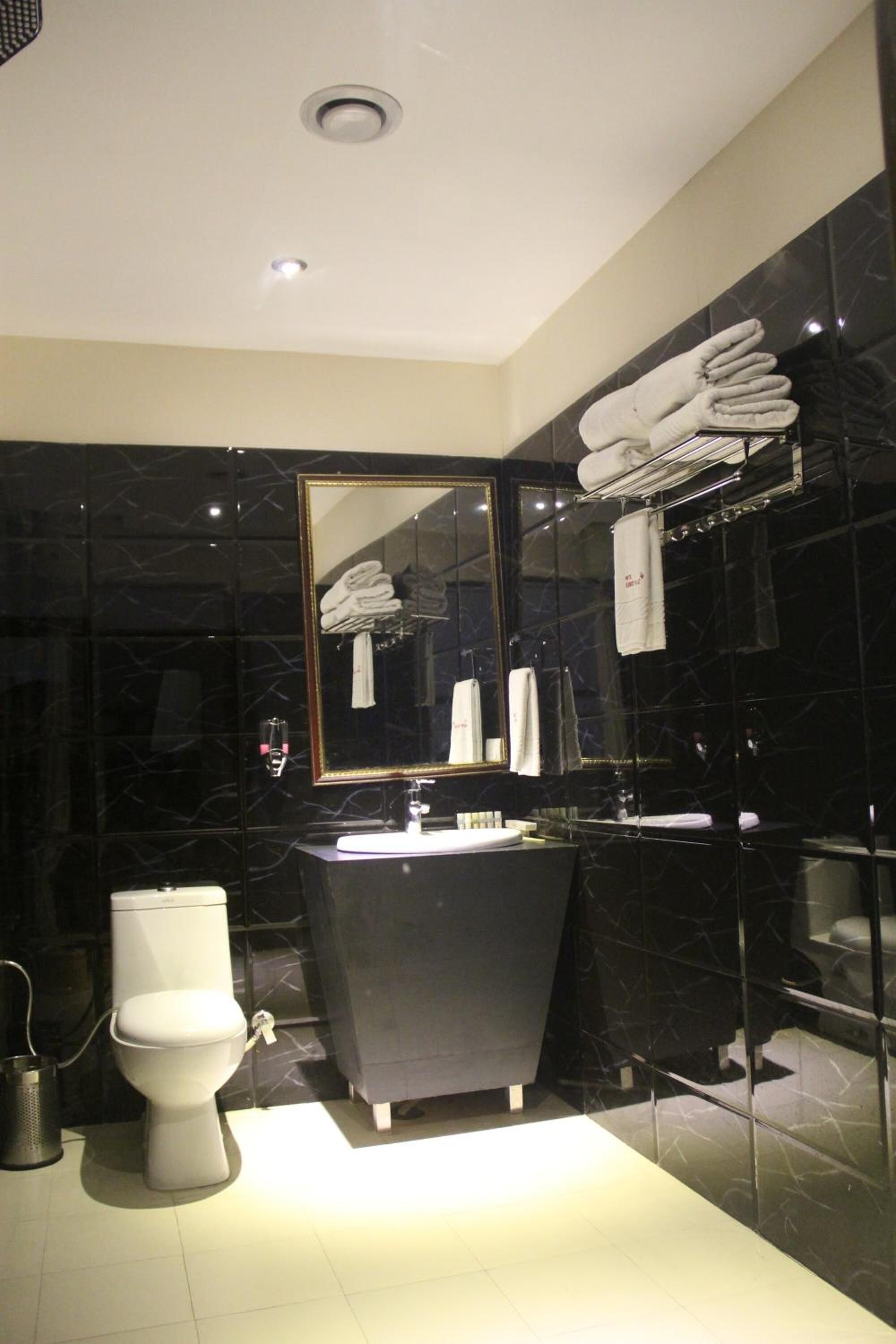 Ein modernes Badezimmer mit schwarzer Marmorwand, Toilette in Weiß, schwarzem Waschtisch und einem großen Spiegel.