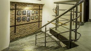 Una escalera con barandillas de metal, un muro de ladrillo con cuadros enmarcados y un candelabro.