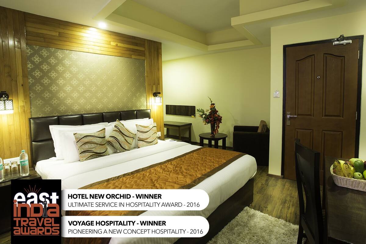 A hotel room with a large bed, wooden headboard, and a small side table with a vase.