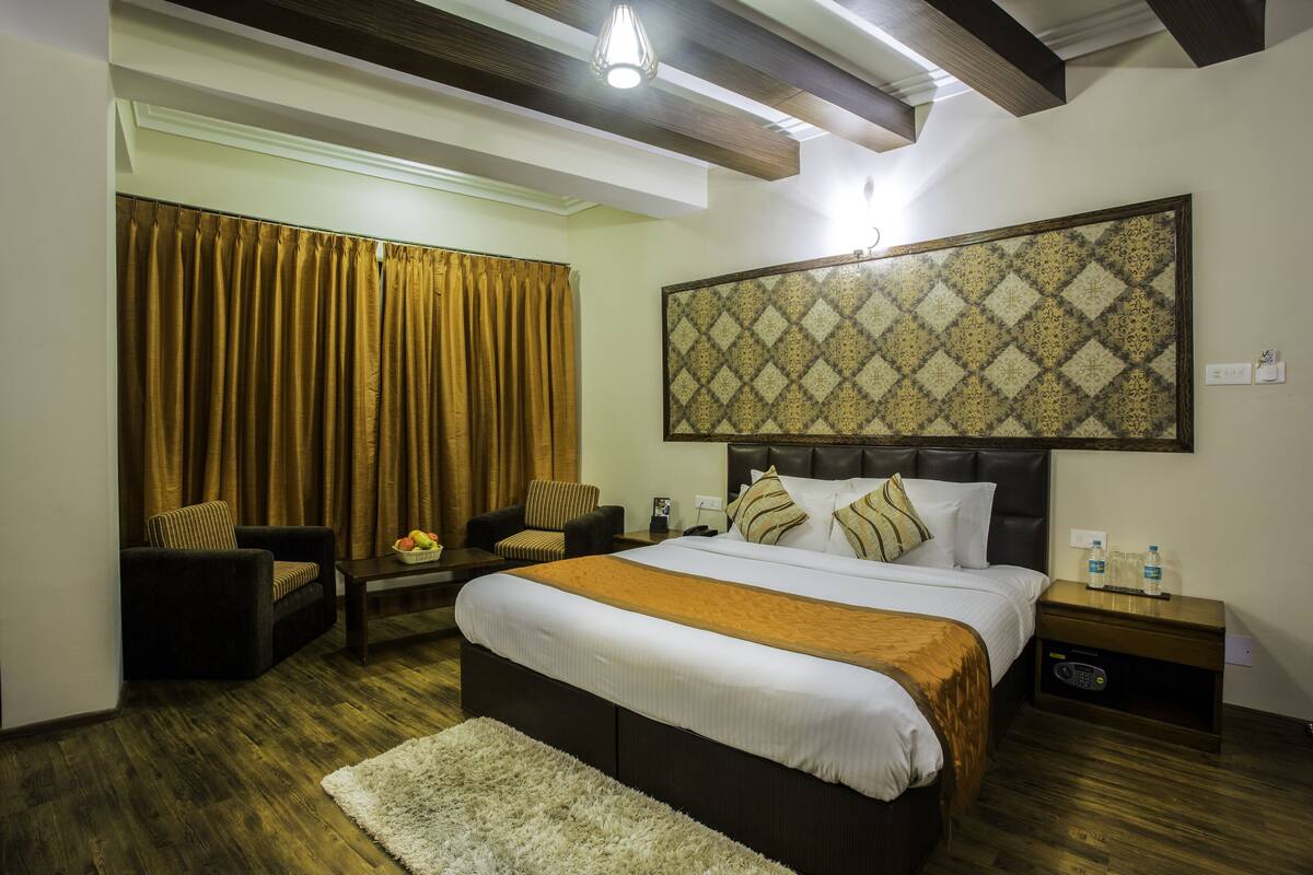 A hotel room with a large bed, a headboard with a patterned design, a wooden ceiling, and a large window with curtains.