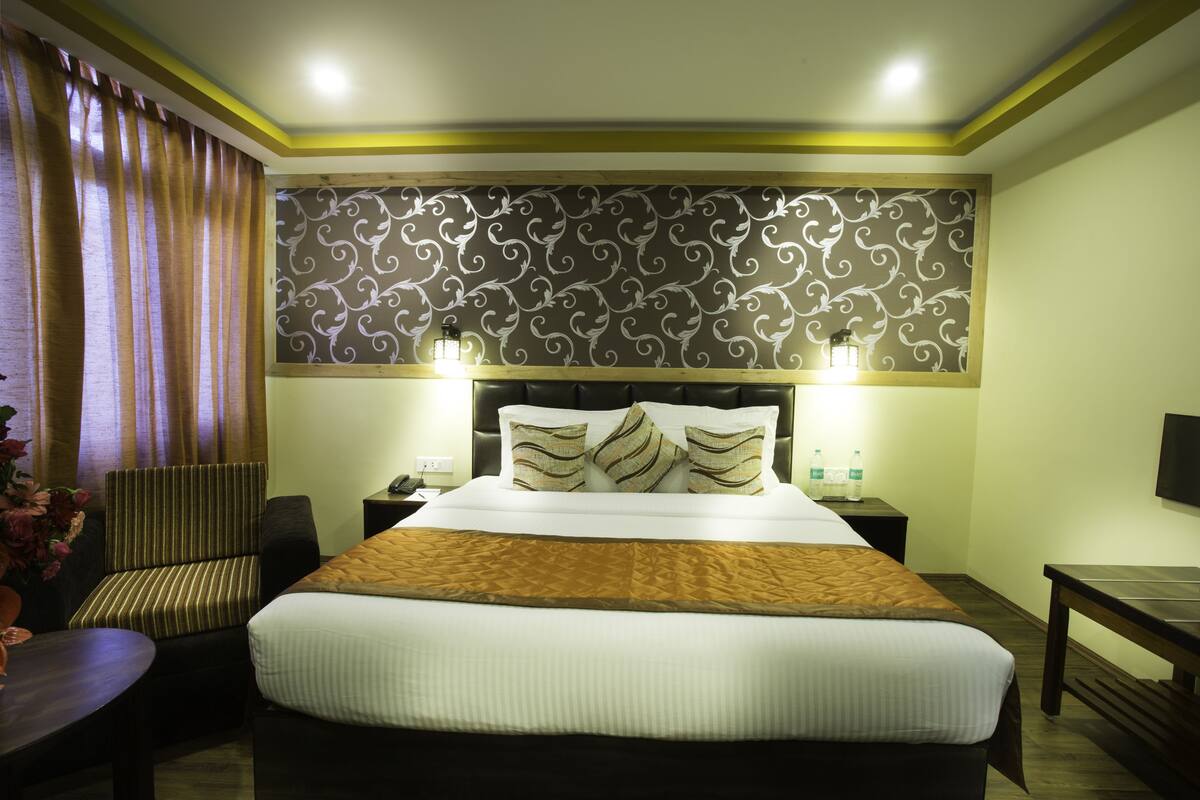 A hotel room with a large bed, a chair, a desk, and a wall-mounted TV.