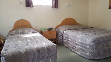 Une chambre avec deux lits simples, une petite table de chevet avec une radio et des mouchoirs, et une fenêtre avec des rideaux.