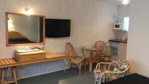 A compact room with a bed, a desk with a computer, a television, and a kitchenette.