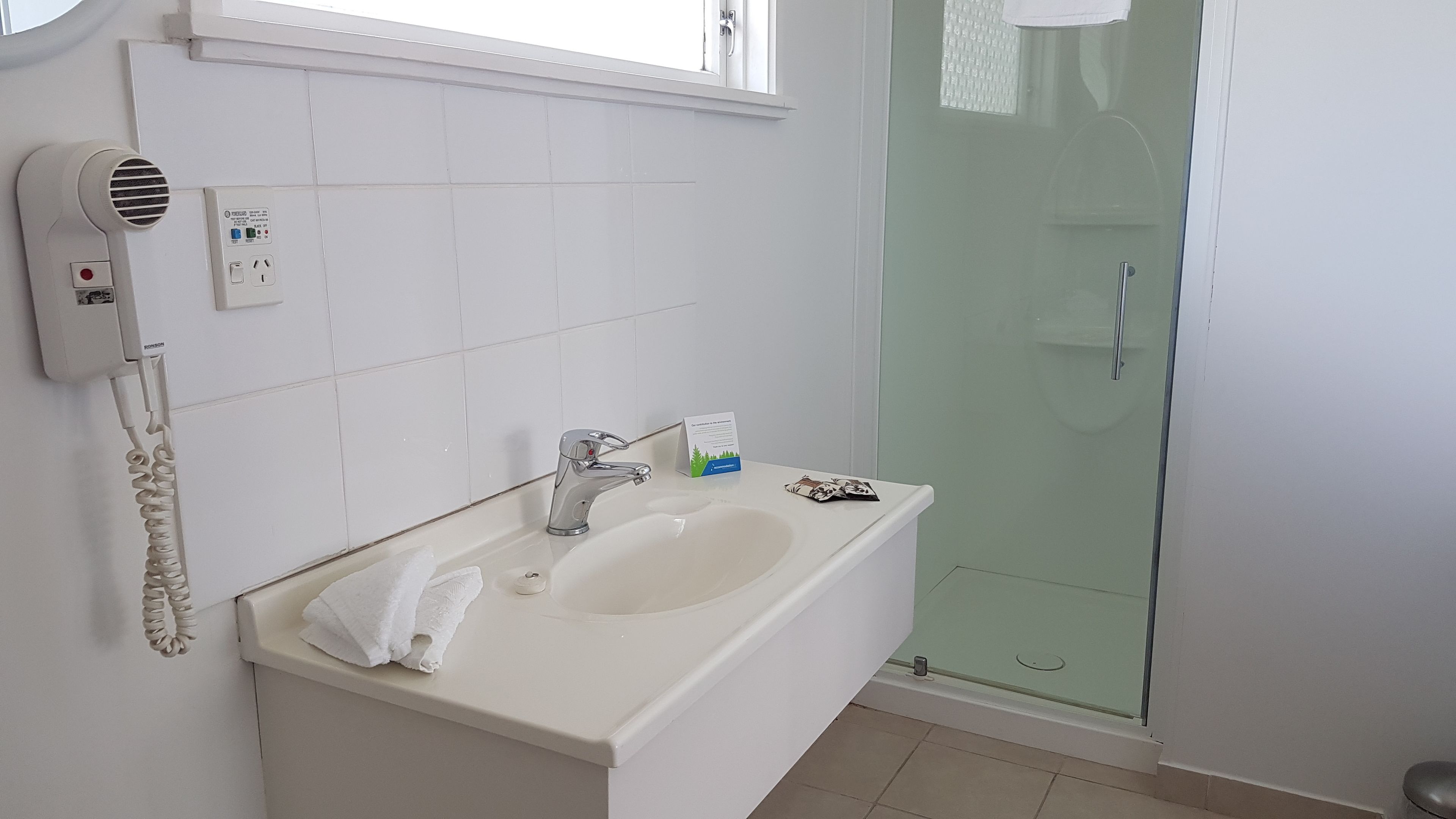 A bathroom with a white sink, a hairdryer, and a glass shower enclosure.