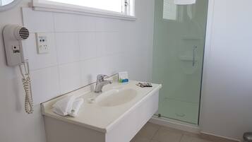 A bathroom with a white sink, a hairdryer, and a glass shower enclosure.