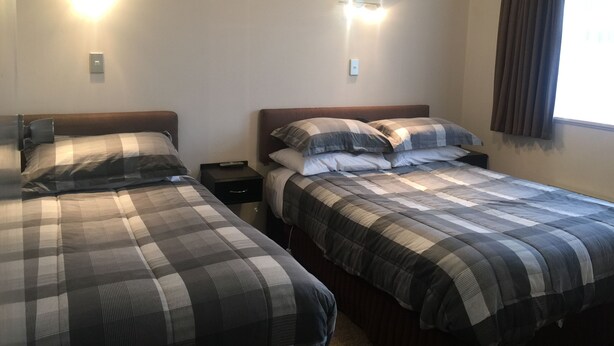 Two single beds with checkered bedding, bedside tables, wall-mounted lights, and a window with curtains.