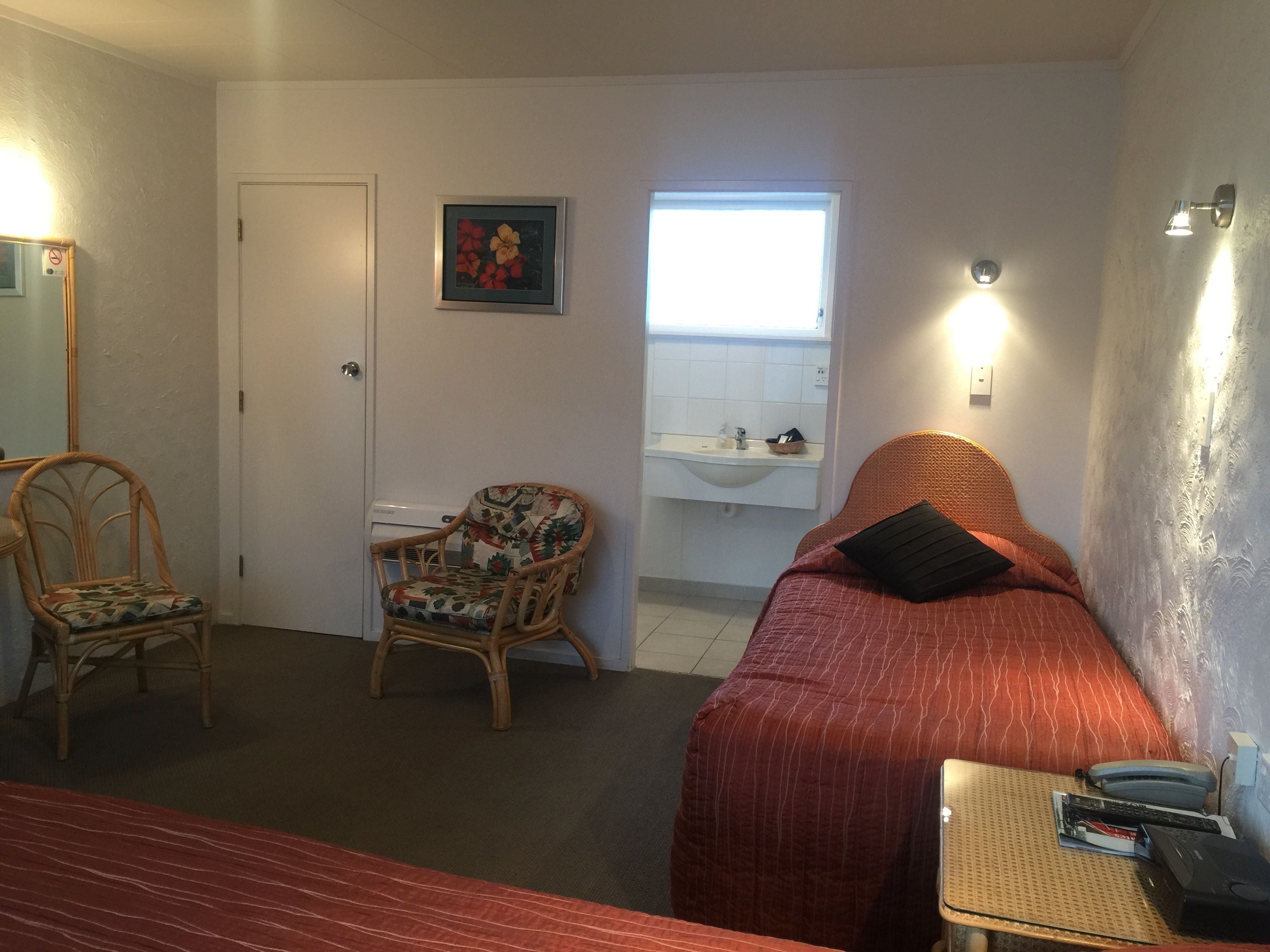 A room with a bed, a chair, a small table, a sink, and a window.