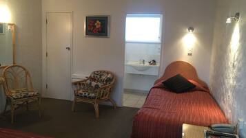 A room with a bed, a chair, a small table, a sink, and a window.
