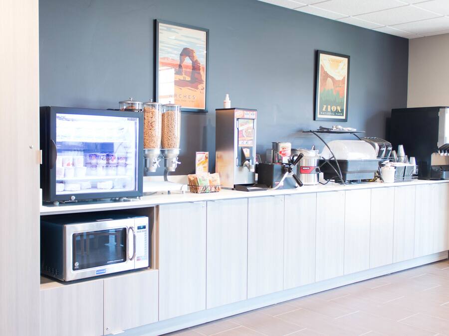 Una barra de desayuno autoservicio con microondas, máquina de café y diferentes dispensadores de alimentos.