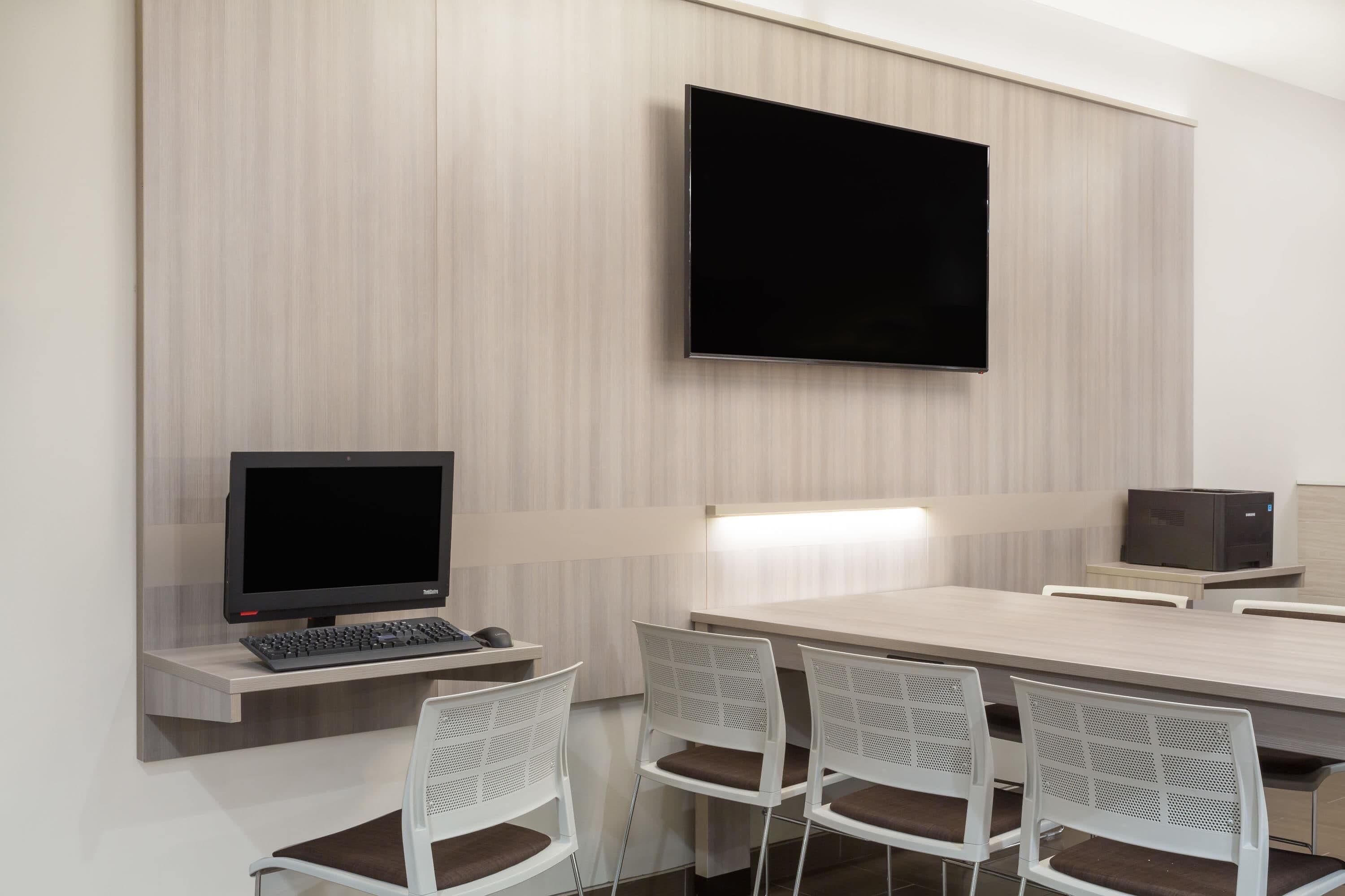 Une salle de conférence équipée d’un téléviseur à écran plat, d’un ordinateur de bureau et d’une longue table entourée de chaises blanches.