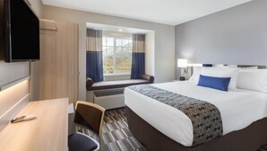 A hotel room with a bed, a desk, a TV, a window with curtains, and a view of the outdoors.