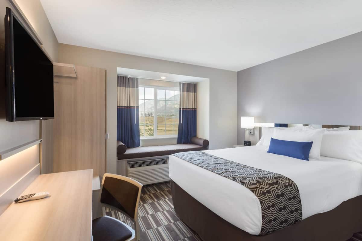 Ett hotellrum med en säng, ett skrivbord, en tv, ett fönster med gardiner och utsikt över omgivningarna.