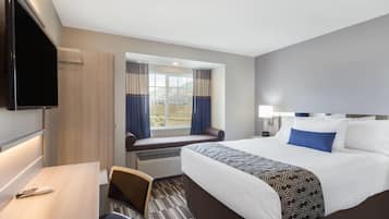 A hotel room with a bed, a desk, a TV, a window with curtains, and a view of the outdoors.