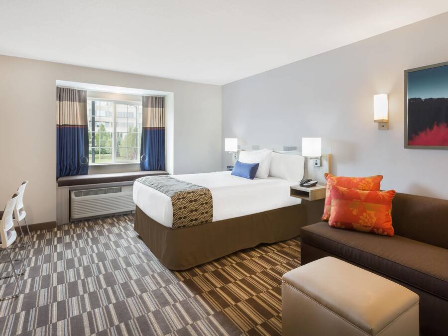 A hotel room with a bed, a sofa, a desk, a chair, and a window with curtains.