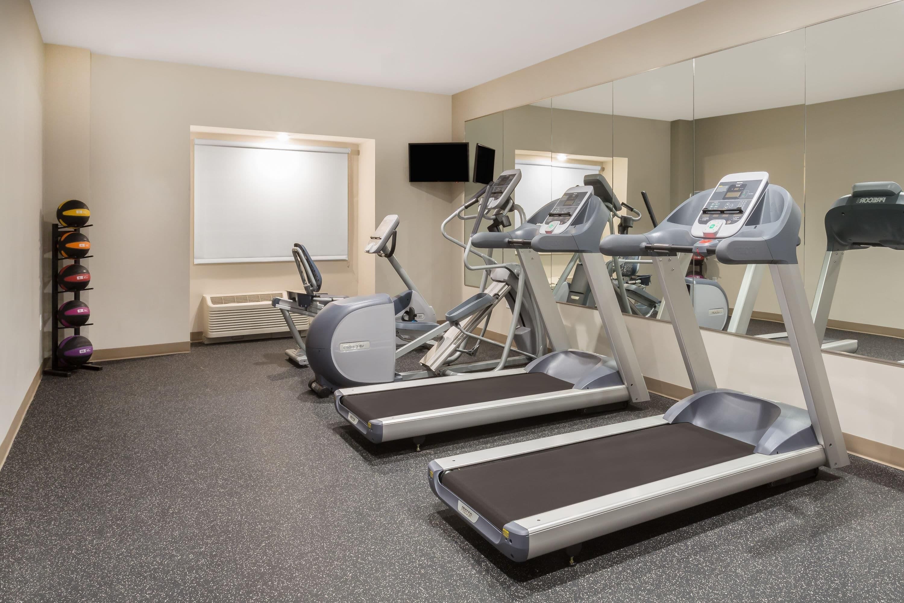 A gym with treadmills, elliptical machines, and a wall-mounted TV.