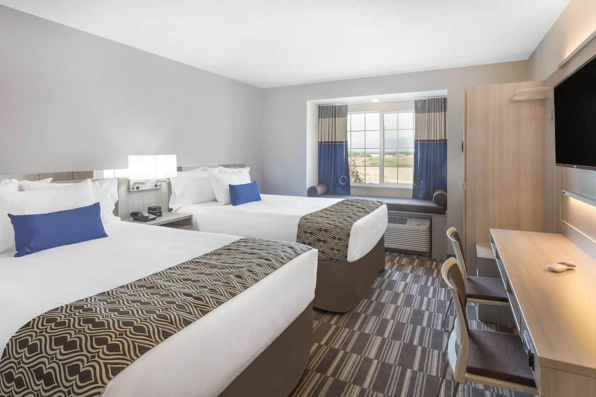 Ett hotellrum med två sängar, ett skrivbord, en stol, en TV och ett fönster med gardiner.