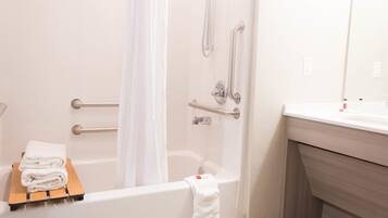 Un bagno moderno con vasca, doccia e mobile lavabo con specchio. Sono presenti maniglie di sostegno nella doccia e un portasciugamani con asciugamani.