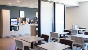 A modern dining area with tables and chairs, a kitchen area with appliances, and large windows providing natural light.