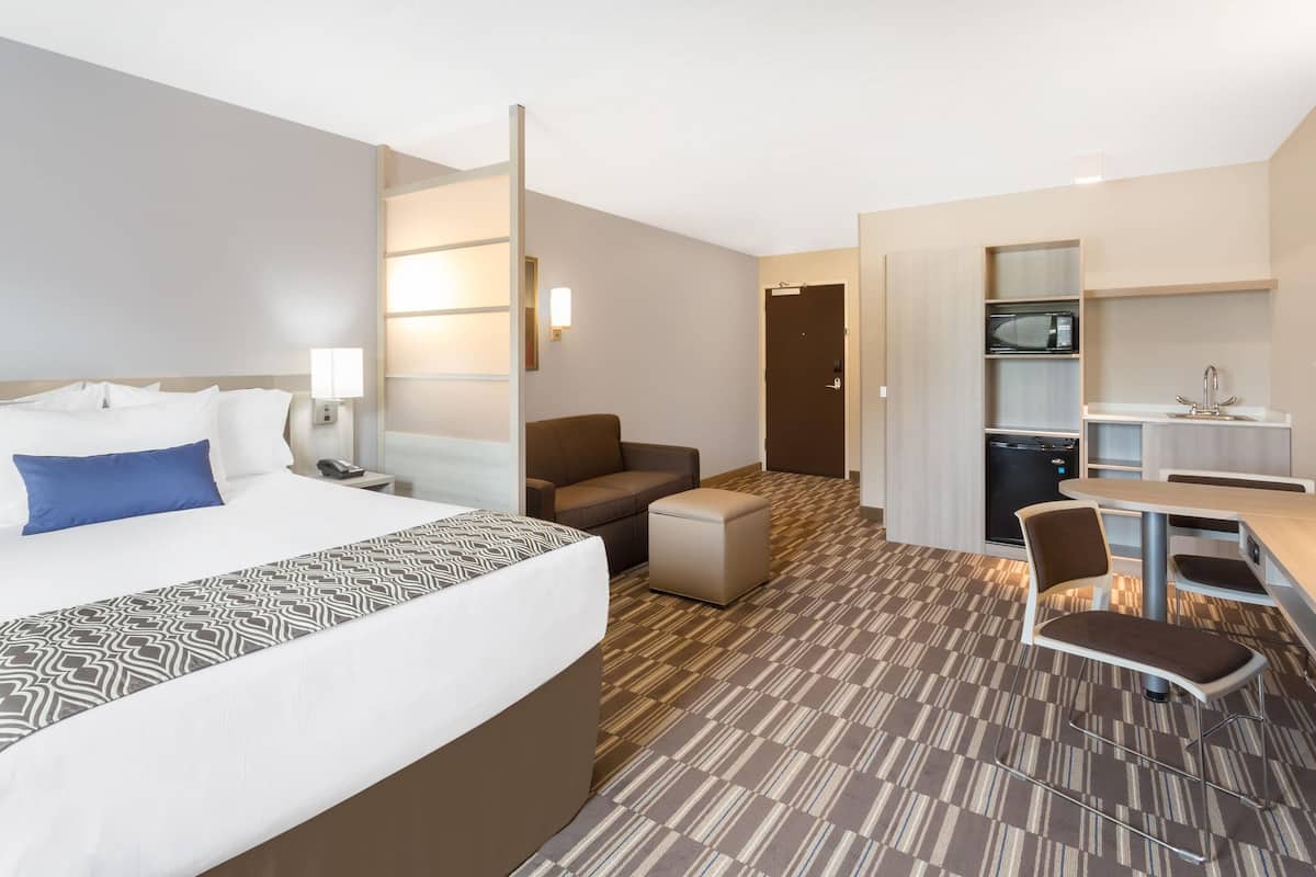 Ett hotellrum med en säng, ett skrivbord, en stol, en soffa, en mikrovågsugn och ett litet pentry.