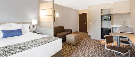 Habitación de hotel con cama, escritorio, silla, sofá, microondas y una pequeña kitchenette.