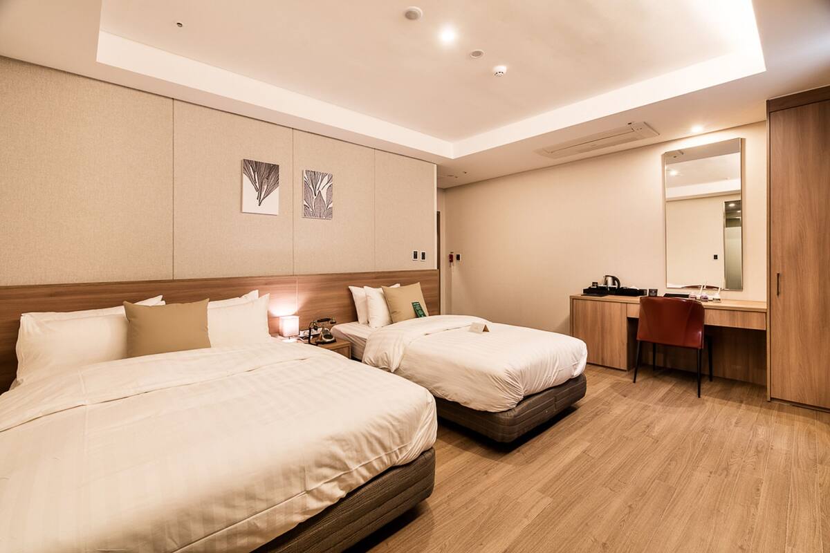 A hotel room with two beds, a desk, a chair, a mirror, and artwork on the wall.