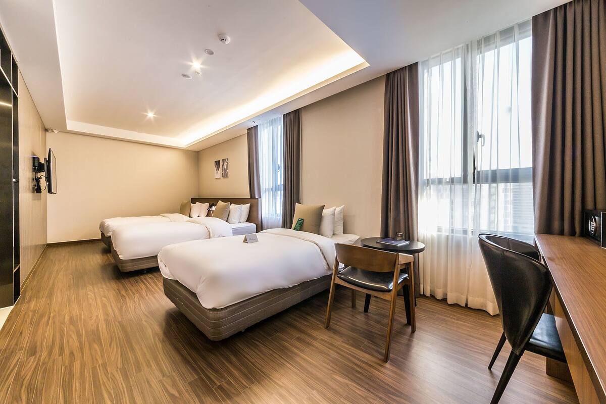 A hotel room with two beds, a desk, a chair, and a large window with curtains.