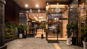 Esterno di un hotel dal design moderno, con ingresso in vetro e piante in vaso.