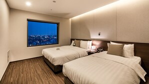 Camera d'albergo con due letti, un comodino, una finestra con vista sulla città e pavimento in legno.