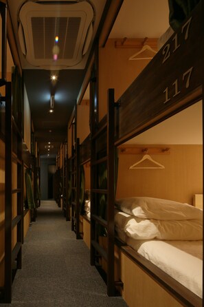 A narrow corridor with bunk beds, each with a numbered hanger, leading to a room with a bed and a hanging coat rack. - iloha Hostel Namba Shinsaibashi (Osaka)