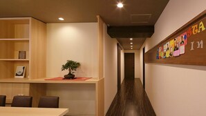Un interior moderno con un largo pasillo, estanterías de madera, una pequeña mesa con sillas y una planta en maceta.