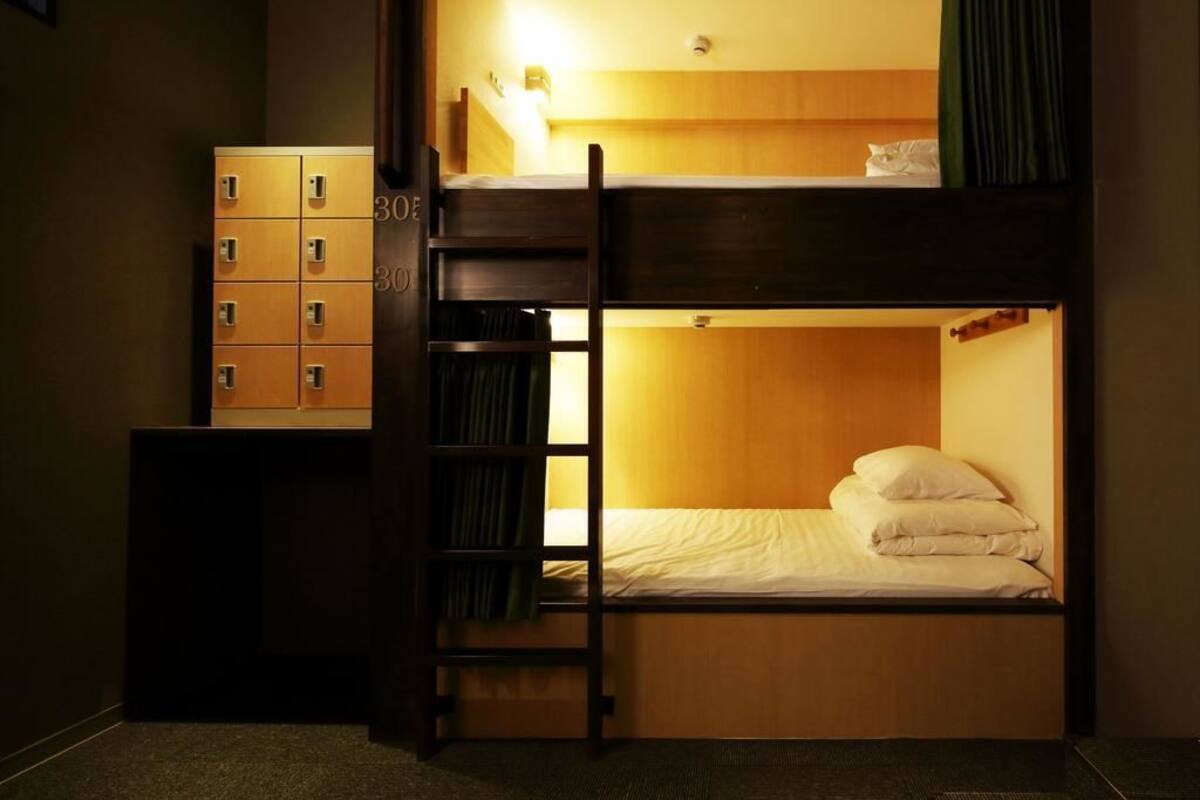 A bunk bed room with a wooden ladder, a small cabinet with multiple drawers, and a single bed with pillows.