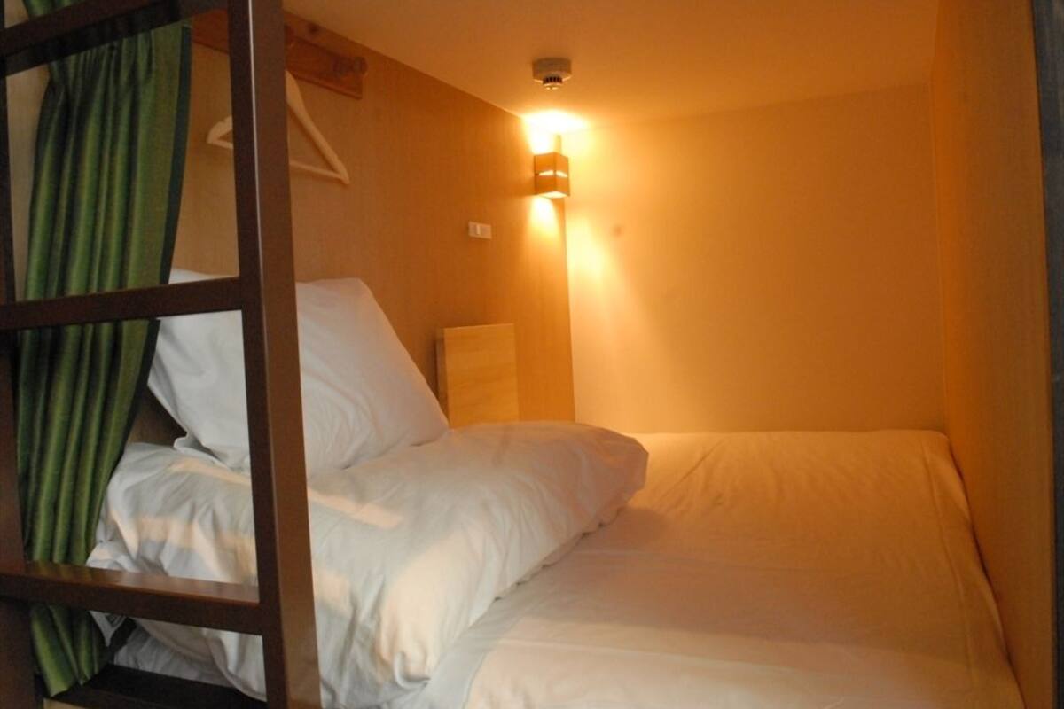 A single bed with white bedding in a room with wooden walls and a green curtain.