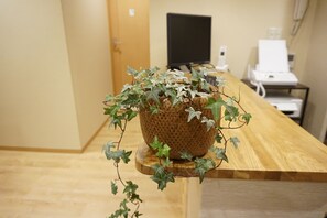 A wooden reception desk with a woven basket containing a potted plant with green leaves. - Hostel Rakutsuki (Osaka)