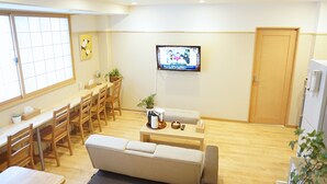 Un salon moderne comprenant un canapé, une table basse, un téléviseur fixé au mur et un coin repas avec des chaises et une table.